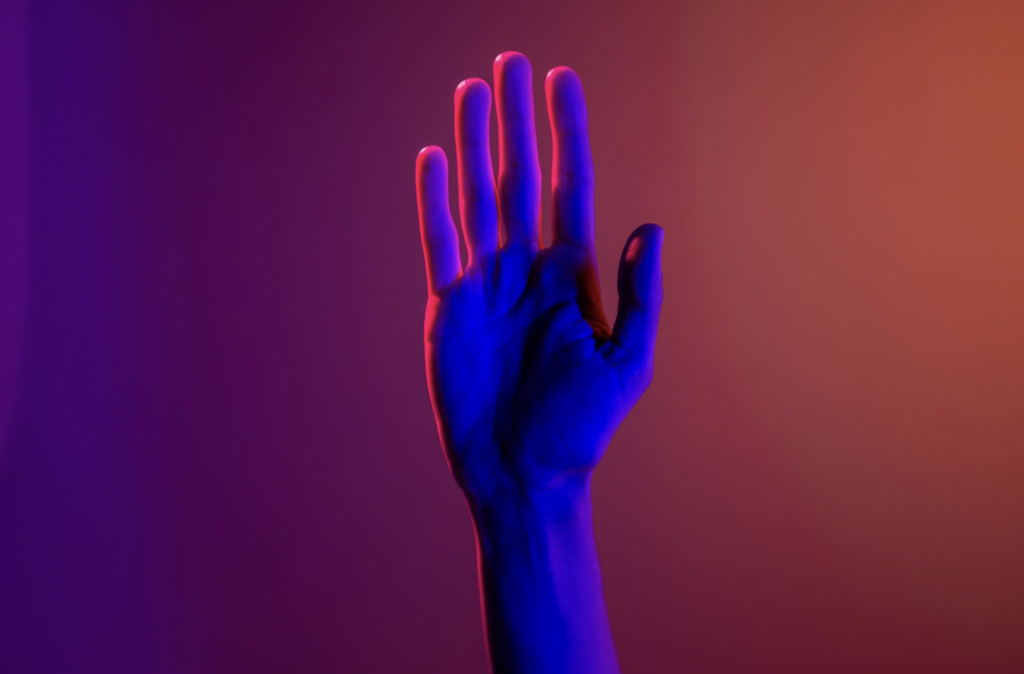 A raised hand in front of an orange and purple background