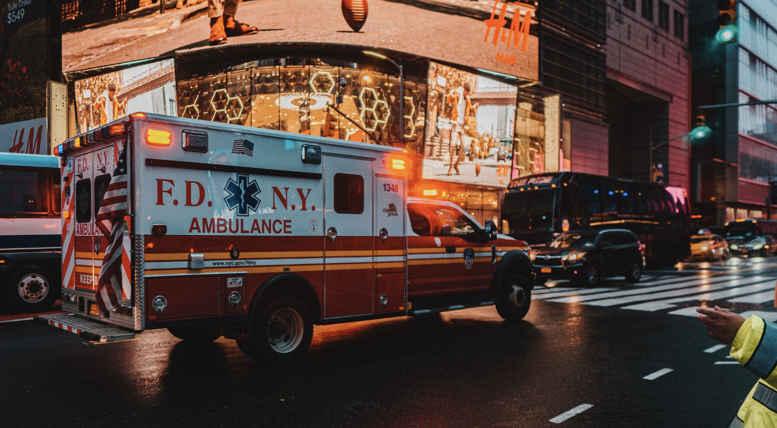 An ambulance driving through a city at dusk.