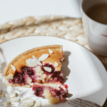 A piece of cherry pie on a plate next to a cup of coffee
