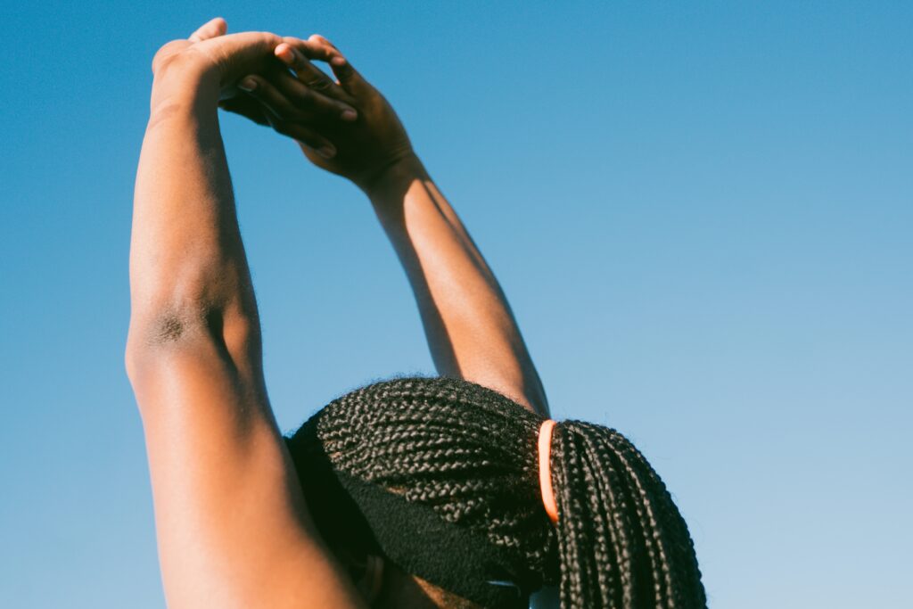 A women with braids stretching her hands above her head.