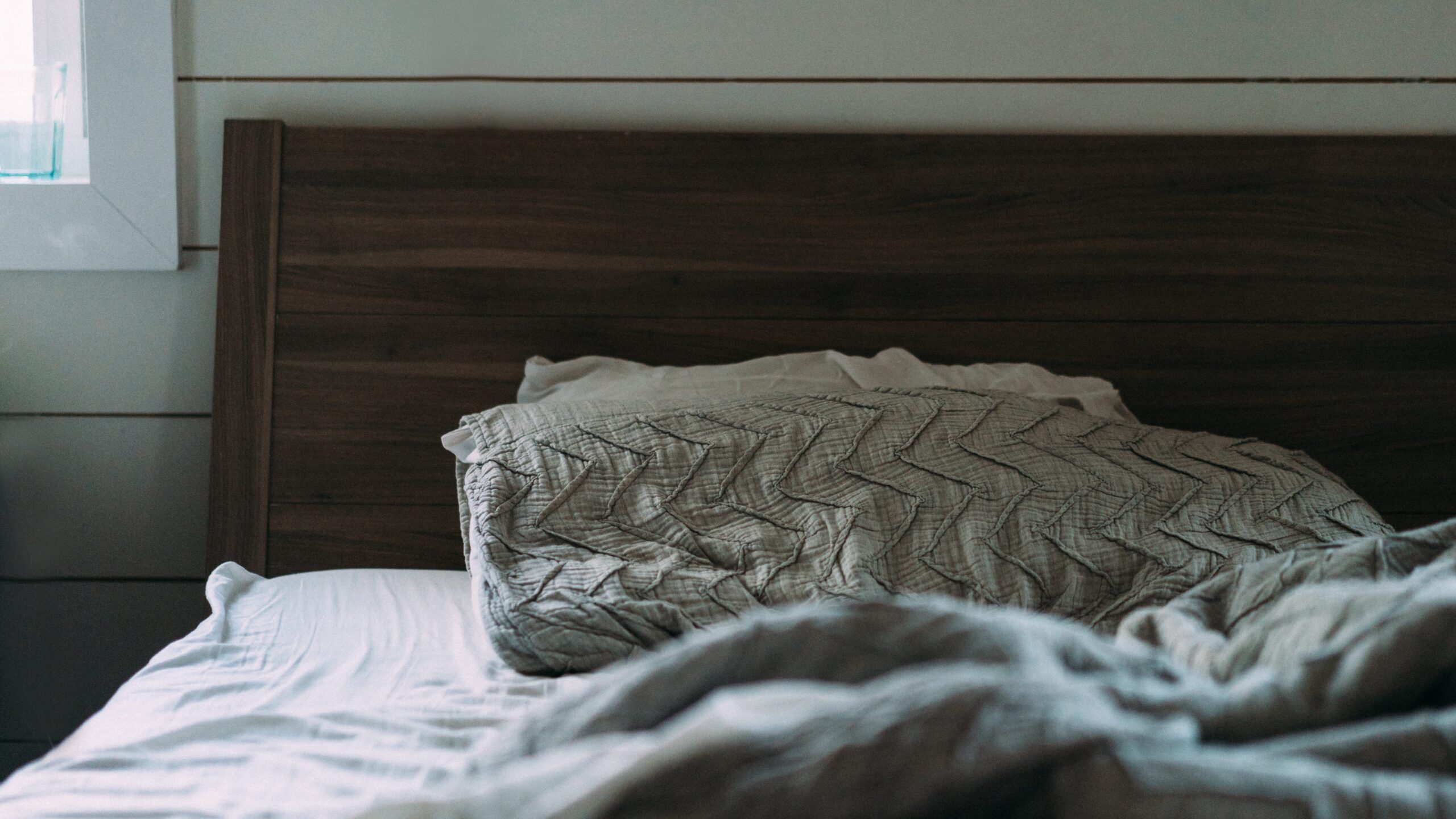 Headboard of a brown wooden bed with rumpled sheets and pillows