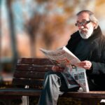 Elderly man reading a newspaper on a bench