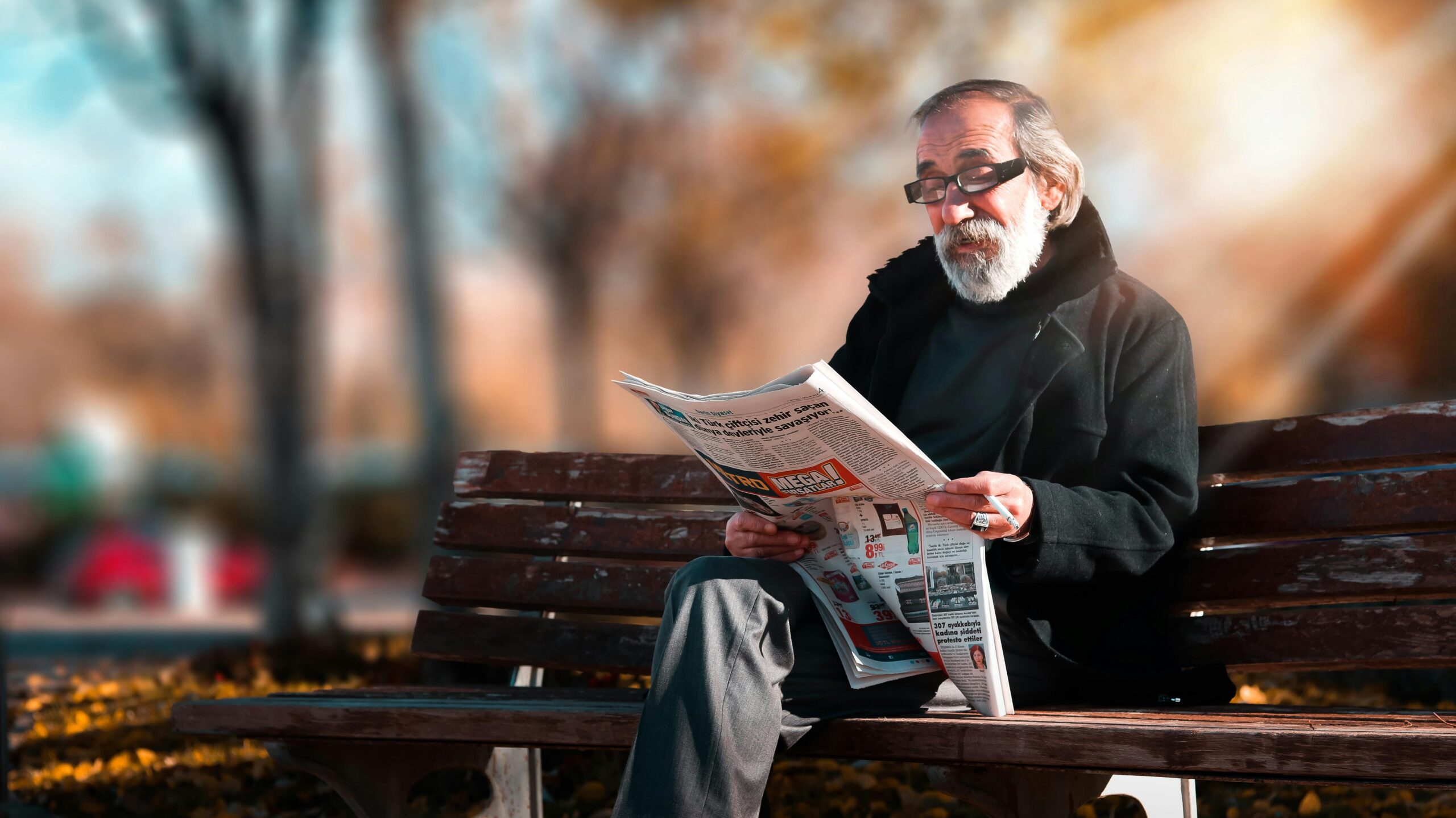 Elderly man reading a newspaper on a bench