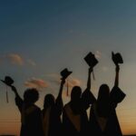 Silhouette of people in graduation gowns holding up their caps