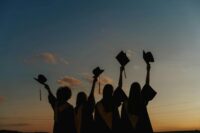 Silhouette of people in graduation gowns holding up their caps