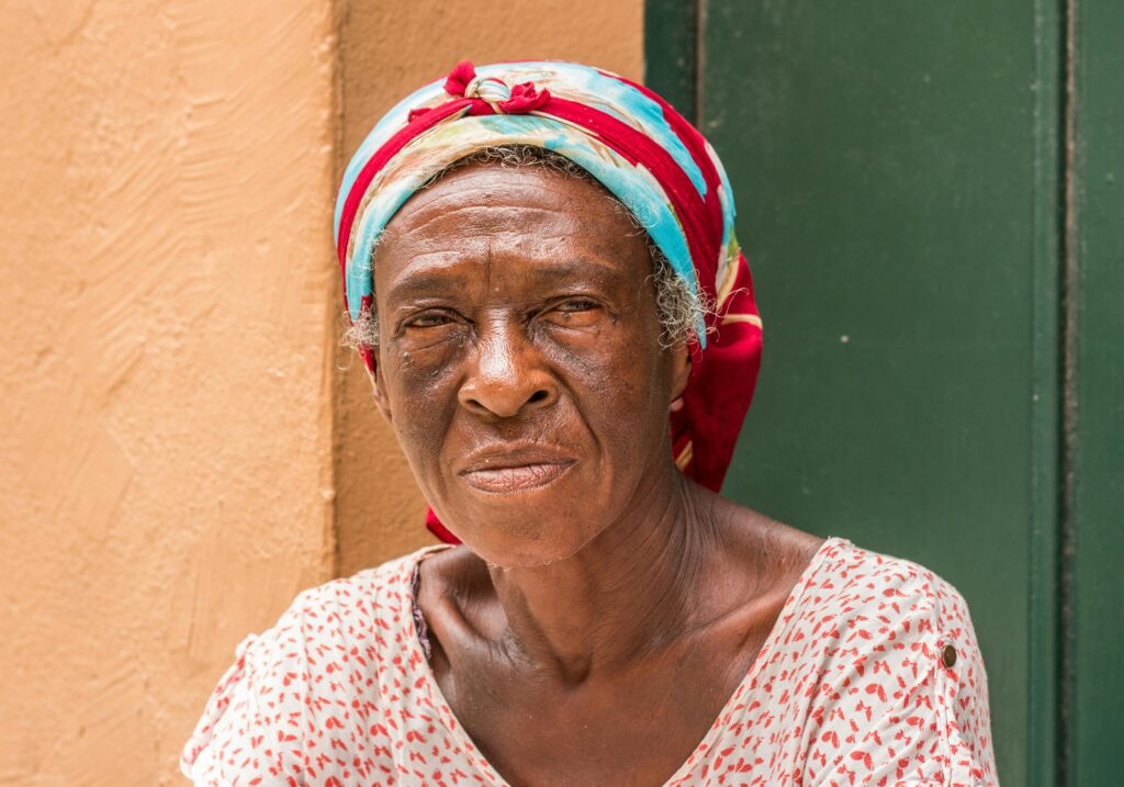 Elderly Black woman in a colorful head scarf and white and red dress