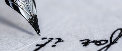 Old-fashioned ink pen poised above a parchment paper on which the words "for it" are visible.