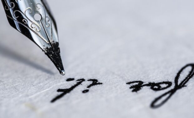 Old-fashioned ink pen poised above a parchment paper on which the words "for it" are visible.