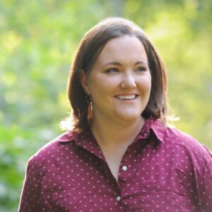 Author Adrienne Kisner, a woman with a red shirt against a green landscape background.