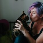 A woman with purple hair kissing a cat.