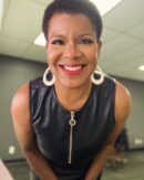 Photo of Tananarive Due, a smiling Black woman with big gold hoop earrings in a leather dress leaning toward the camera and smiling.