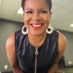 Photo of Tananarive Due, a smiling Black woman with big gold hoop earrings in a leather dress leaning toward the camera and smiling.