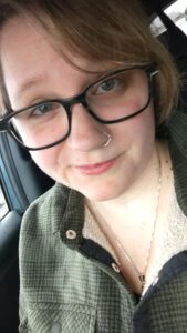 Bethany Willard, a white woman with black glasses, a nose ring, and a knowing grin.