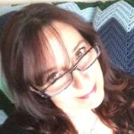 A white woman with glasses and brown hair smiling up at camera