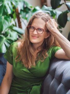 Photo of Laura Stanfill, a woman with blond hair and glasses, wearing a green shirt and smiling