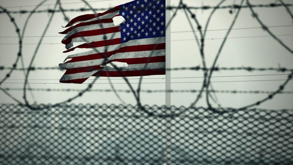 An American flag behind a detainment fence